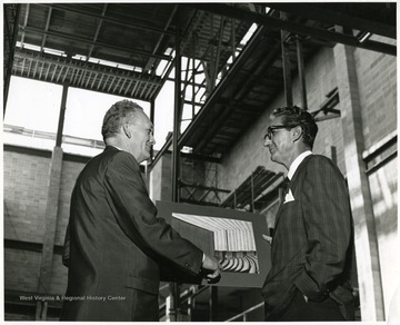 A portrait of Dean Duncan (right), from the Creative Arts Center, examining and discussing a photograph with another man during construction.