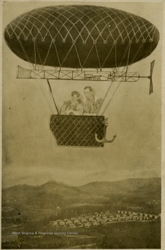 A blimp in the air with two males in a basket flies over a city view: a composite photo.