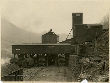 A photograph of coal processing buildings outside a mine with coal train cars underneath.
