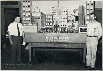 A photograph of two men standing next to a model advertising the Weston Fire Department.