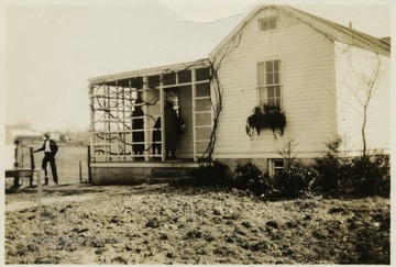 A photograph of what appears to be a home, with people on the porch and a man standing in the yard.