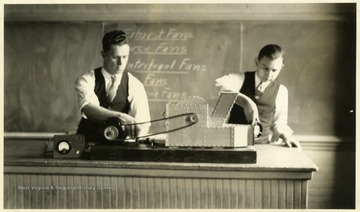 A photograph of two men in a classroom working with a piece of laboratory equipment.