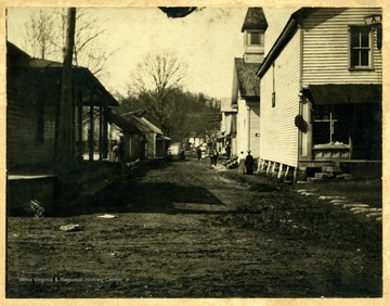 'Left Side: W. A. Colerider's Saddle & Harness Shop; Ross Miller's Cabinet Work Shop; Lewellyn Buckhausen's Shoe Shop; Doctor's Office and Post Office; On Right Side: A. N. Singer's Store; M. E. Church; First Post Office; Doctor's Office; Tower Hall; Miller Store & Telephone Exchange; Old Buntin Home; Lloyd Talbott Home and H. B. Darnall Home.'