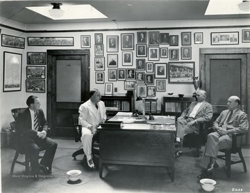 A photograph of Koepler at his desk with three other individuals. 'Notice; Permission is granted to reproduce this photograph only on condition that each reproduction shall bear the following credit line; Photograph by Norfolk &amp; Western Railway'