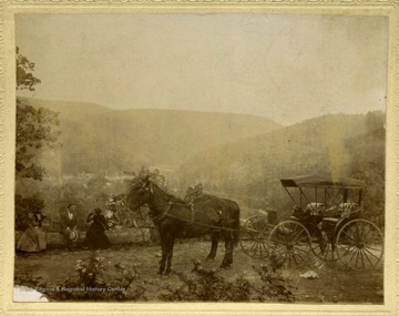 A Horse drawn carriage and passengers out in a scenic mountain view.