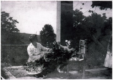 A photograph of a woman seated with a child as they examine a bunch of flowers in a vase.