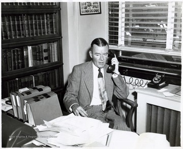 A photograph of John Sanders seated at his desk and talking on the phone.