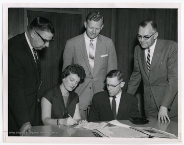 "Evelyn L. K. Harris and Frank J. Krebs are shown in April, 1958 signing a contract for preparation of manuscript for the book, 'From Humble Beginnings, W. Va State Federation of Labor, 1903-1957.' E. A. Carter, Benjamin W. Skeen and Glen Armstrong (standing, left to right), members of the Trustees and Editorial Board of the W. Va Labor History Publishing Fund, look on."