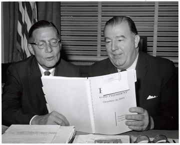 A photograph of Senator Randolph (right) seated with an unidentified man looking at a Report of the President's Council on Aging.