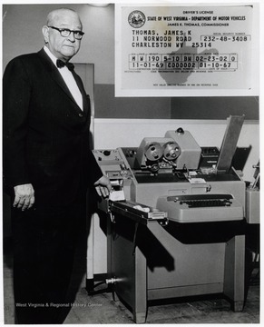 A photograph of James Thomas standing next to a machine that produces driver's licenses.