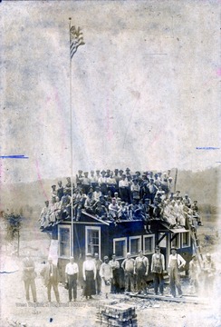 A photograph of an unidentified group of workers gathered outside, and on top of, a small building.