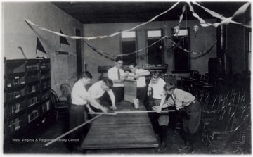 A photograph of a group of male students gathered at a table working on a project using wood and tools. The classroom is decorated with streamers.