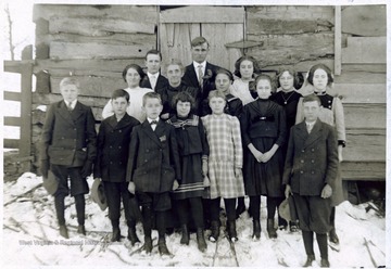 'This picture was taken of my Sabbath School class December the 1912 Christmas in the afternoon. The log stable back of the group was built from the logs taken from the old Selby School house, built prior to 1844. Willie Board, Superintendent, M. J. Henry, teacher; the names of the class: Joe Fleming, Charles Morison, Dane Pixler, Nelson Shafer, Benny Jolliff, Dimple Lazzell, Clarrissa Jones, Mabel Fields, Bertha Runner, Renna Pixler, Ida Shafer, Ethel Runner, Peril Maxin'