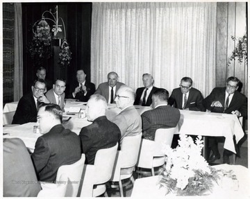 A photograph of a gathering of West Virginia politicians. Herman Walker (far table, right), Governor Hulett C. Smith (far table, third from right), Dyke Raese (far table, third from left), Jennings Randolph (far table, second from left), Paul Miller (far table, left), Howard Smyth (foreground, second from left), Elmer Prince (foreground, third from left).