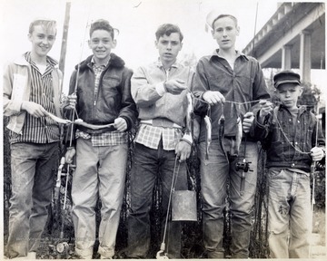 A photograph of a group of young boys showing off the fish that they have caught.