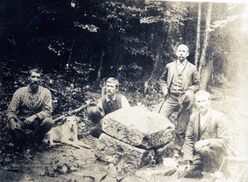 Four unidentified men and a dog, posing with the Fairfax Stone in a wooded area outside Thomas, W. Va. The stone marks the western point of Lord Fairfax's proprietary claim and  the southernmost point on the North-South state boundary line between West Virginia and Maryland.