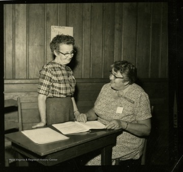Two women examine documents at a table.