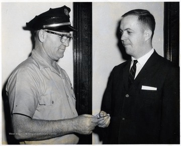 A man in uniform exchanging a small piece of paper with another individual.