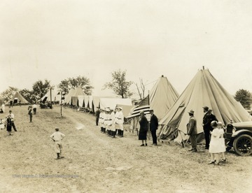A photograph of people standing outside a long row of tents at a campground. Print number 1066.