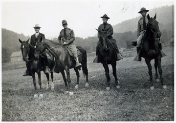 A photograph of three uniformed men and one dressed in civilian clothes seated on horses.