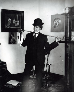 A photograph of a woman dressed in a suit with a hat and a cane.