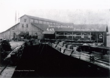 A photograph of a lumber mill, with a group of individuals gathered near the mill's entrance on the left.