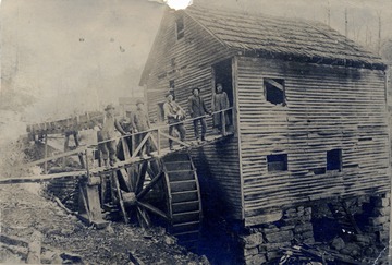 A photograph of an old mill, with a group of workers standing along the walkway to the entrance. 