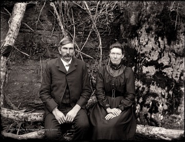A portrait of a couple sitting on branches at the foot of a tree in Helvetia, W. Va.