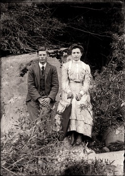 A portrait of a man and women sitting on a boulder.