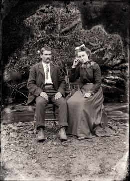 A portrait of a couple sitting on a felled tree.