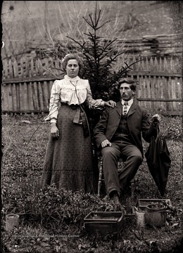 A portrait of a couple taken in front of a small evergreen tree.