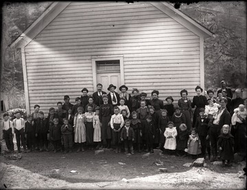 A group of people of different generations gather just outside of a building; they structure could well be a church or a school.