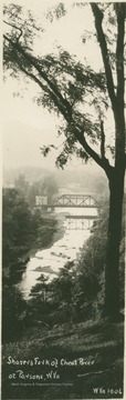 Postcard photograph of a metal bridge crossing Shavers Fork with a building, possible a toll house, on the bank next to the bridge in Tucker County.