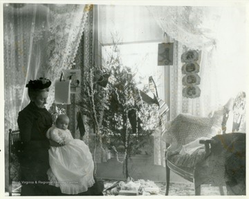 An older woman holding a baby, while sitting near a popcorn draped Christmas tree. 