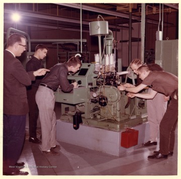 Engineering students demonstrate on a machine while a professor oversees.