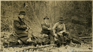 Postcard photograph of three men sitting on a log.
