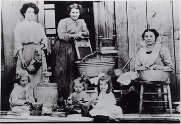 Women and children in the middle of with various household chores such as laundry, and filling kerosene lanterns. The structure is believed to be a boarding house near Hacker Valley, W. Va.