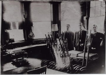 Three men in suits posed behind equipment in a work room.
