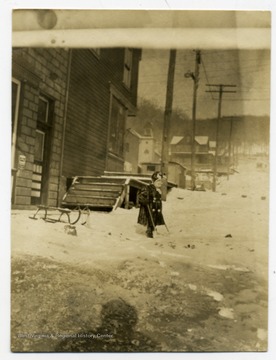 A child explores in the snow with a sled parked behind him.
