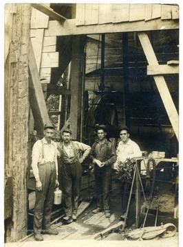 Postcard showing four men standing at the base of an oil well.