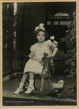 Frances Davenport Packette posing on a rocking horse, on a front porch 
