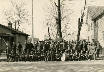 Photograph of possibly an Army unit with flags, drums and some men wearing World War I doughboy helmets.