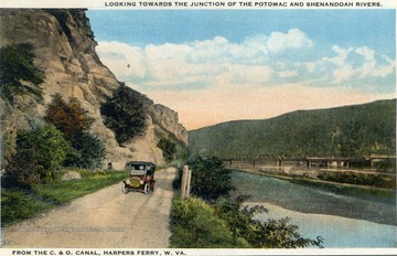Color postcard of a ca. 1918 touring car driving next to the the C&amp;O Canal. The Harpers Ferry bridge crossing the confluence of the Potomac and the Shenandoah Rivers is in the background. 