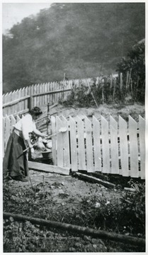 Romanian woman white washing a fence on her property.