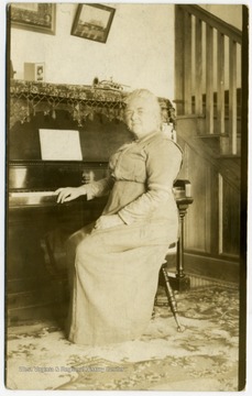 Post card print of May Haldeman sitting at a piano. Note on the back written by May and describes in the photograph in detail. 