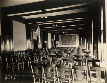 Room with several rows of wooden chairs facing a stage.