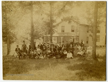 Group portrait of several men, women, and children, many holding instruments, pose outside  "Assembly House".