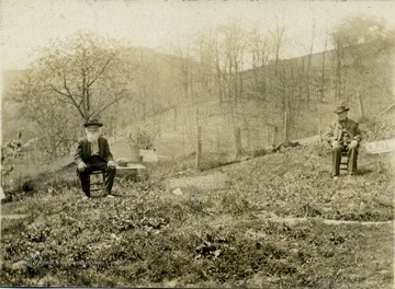 Alfred, left and James, right sit in front of the remains of the old Breakiron  house. Signs label the locations of the out buildings. 