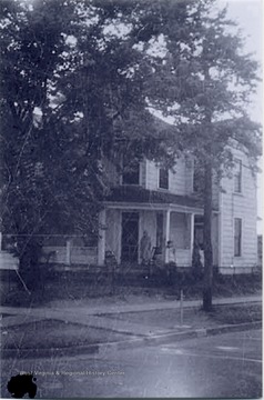 Marie Henry, wife of Frank Henry, is standing on the porch. The house is located on the corner of Third and E Streets.