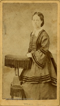 A carte de visite of a young woman, Mama Young, posed on a fringe trimmed chair and wearing mid-19th century style dress and hair.